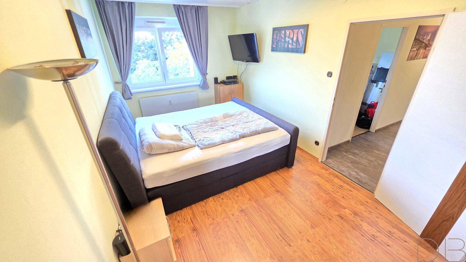 Gemütliches Schlafzimmer mit Holzboden, einem Doppelbett und einem Fenster mit Vorhängen.