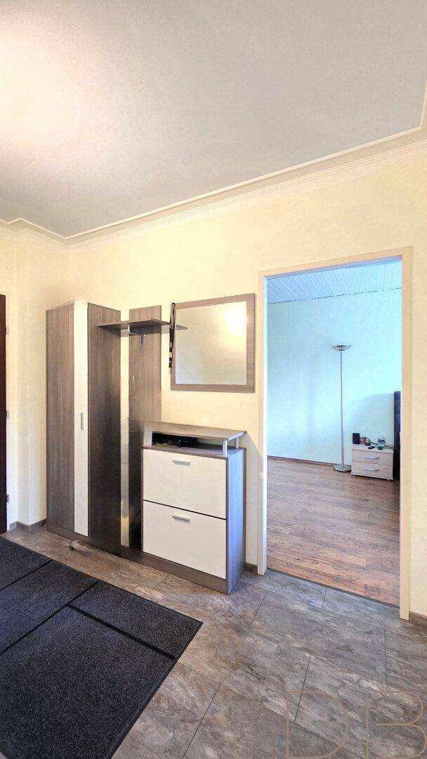 Heller Eingangsbereich mit Fliesenboden, Garderobe und Spiegel, der zu einem Wohnbereich führt.