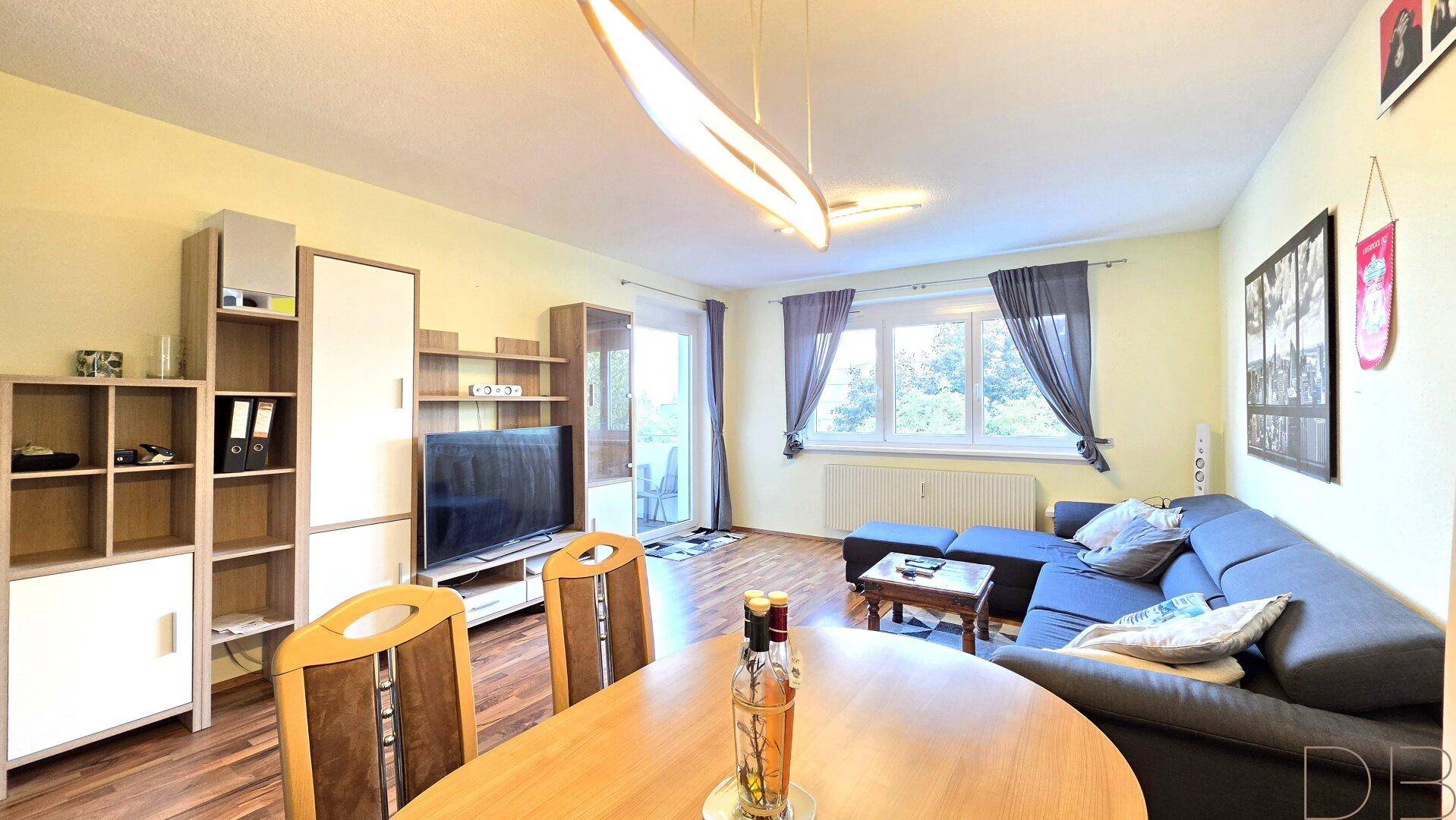 Heller Wohn-Essbereich mit Holzboden, Sofa, Esstisch und großem Fenster.