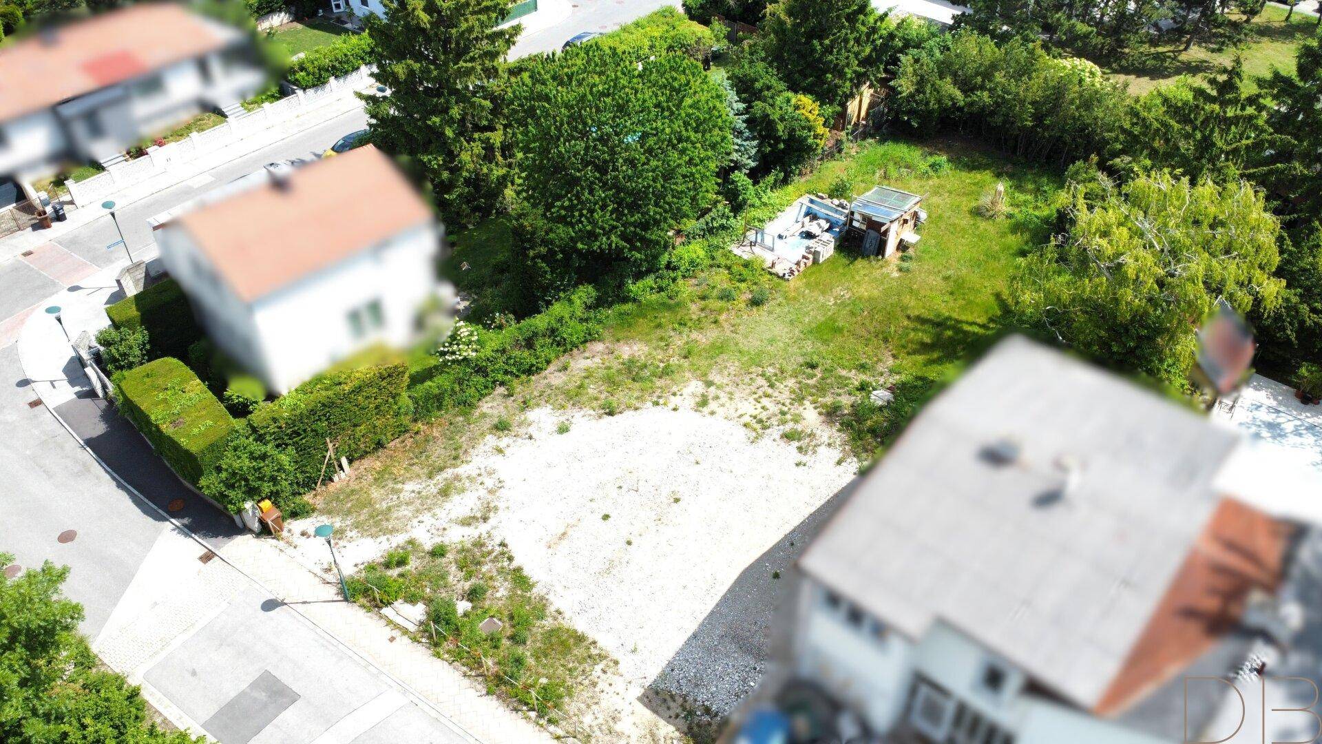 Weitläufiges unbebautes Grundstück mit angrenzender Straße und umgebenden Bäumen, ideal für Neubauprojekt.
