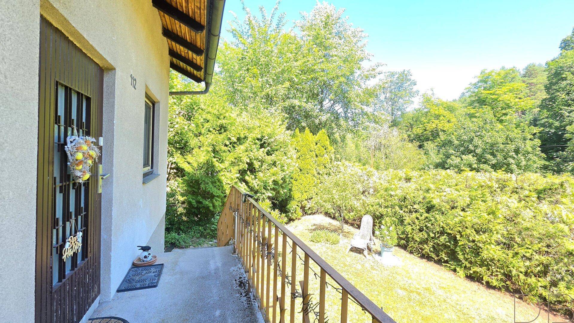Kleiner Balkon am Eingang mit Geländer und Blick auf den grünen Garten.