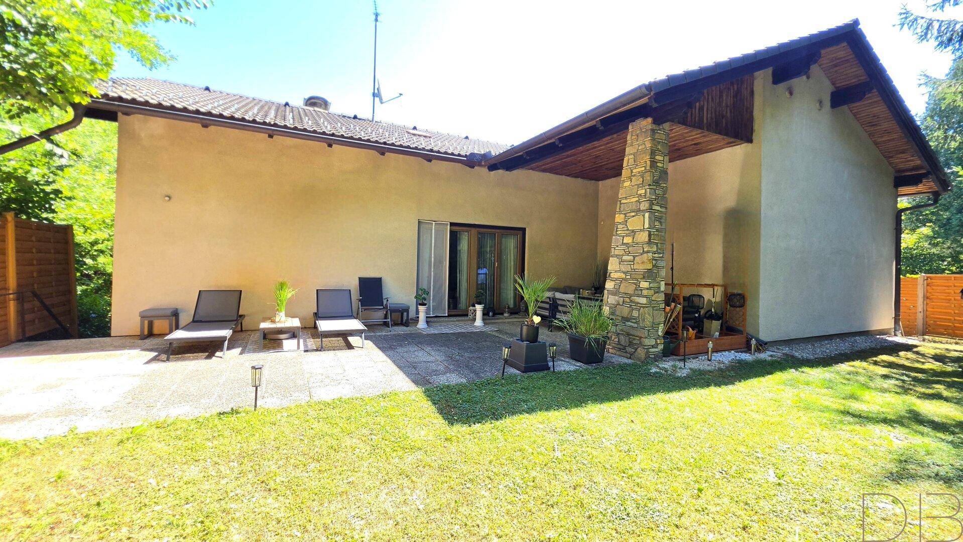 Seitenansicht des Hauses mit weitläufiger Rasenfläche und einer gepflasterten Terrasse.