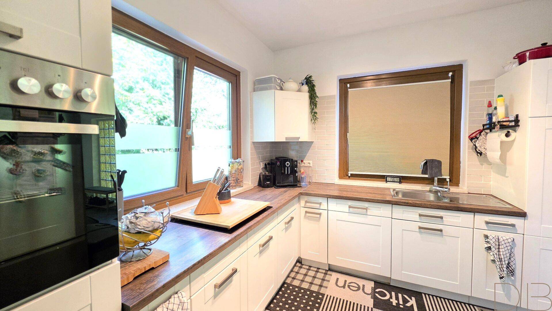 Helle Küche mit weißen Schränken, Holz-Arbeitsplatten und einem Fenster mit Blick ins Grüne.