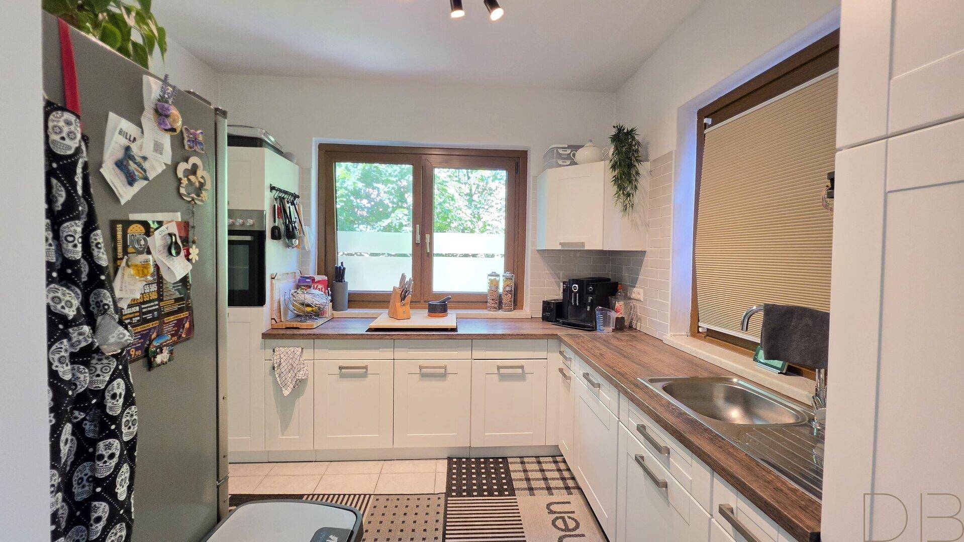 Geräumige Küche mit weißen Fronten, Holz-Arbeitsplatten und integriertem Kühlschrank.