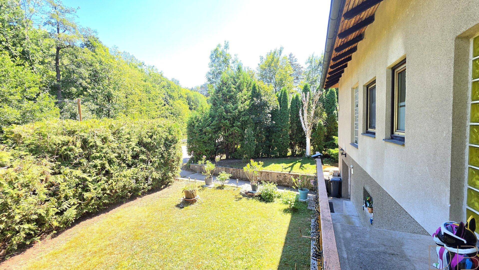 Seitenansicht des Hauses mit einem gepflegten Garten und üppiger Heckenbepflanzung.