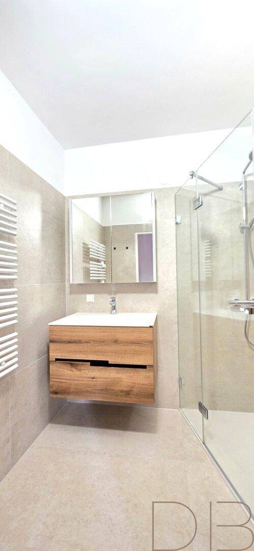 Modernes Badezimmer mit hellen Fliesen, Holzwaschtisch und begehbarer Glasdusche.