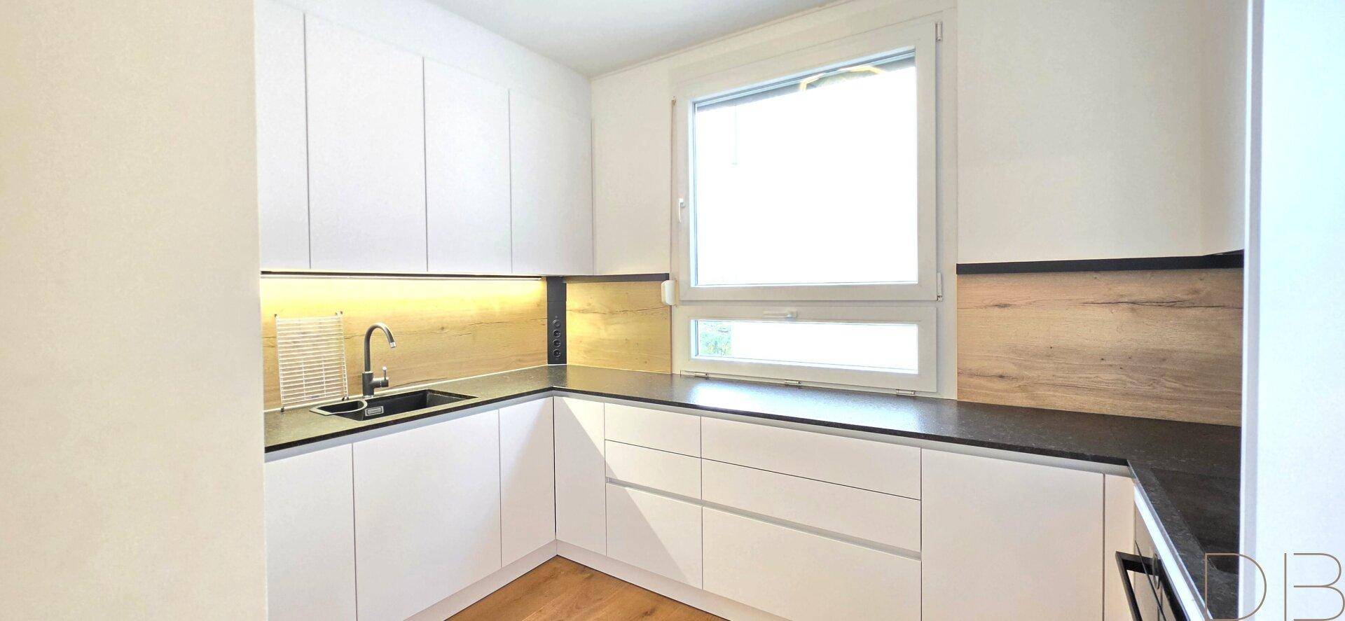 Helle Küche mit weißen Fronten, Holzdetails und dunkler Arbeitsfläche.