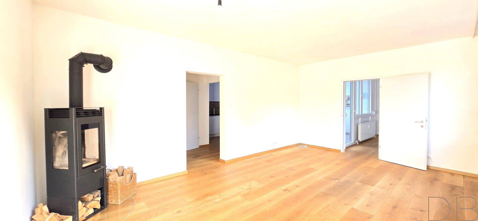 Heller Raum mit Holzboden und modernem Kaminofen, bereit zur individuellen Gestaltung.