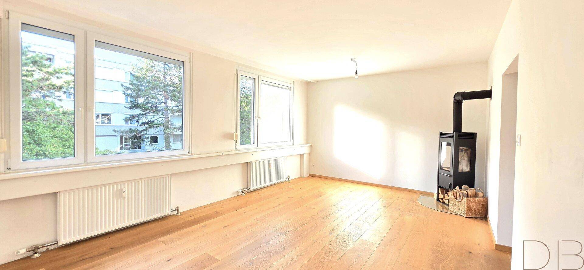 Helles Wohnzimmer mit Holzboden, großen Fenstern und einem modernen Kaminofen.