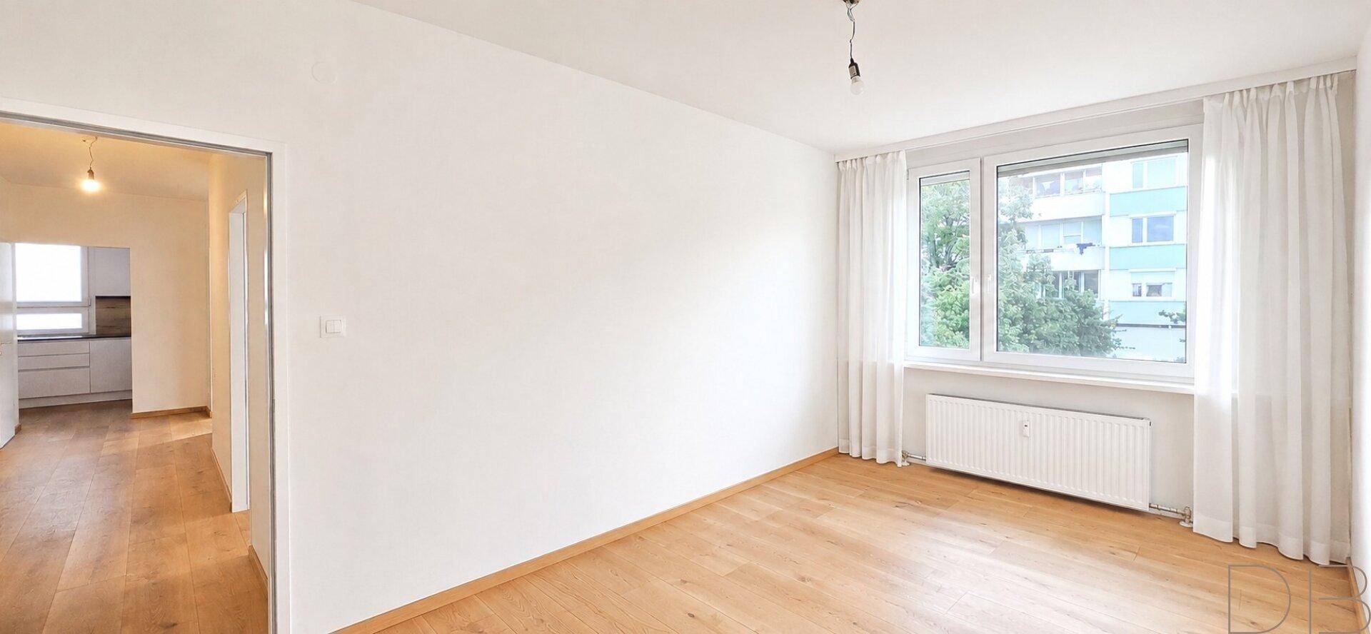 Heller Raum mit großen Fenstern, Holzboden und Blick ins Grüne.