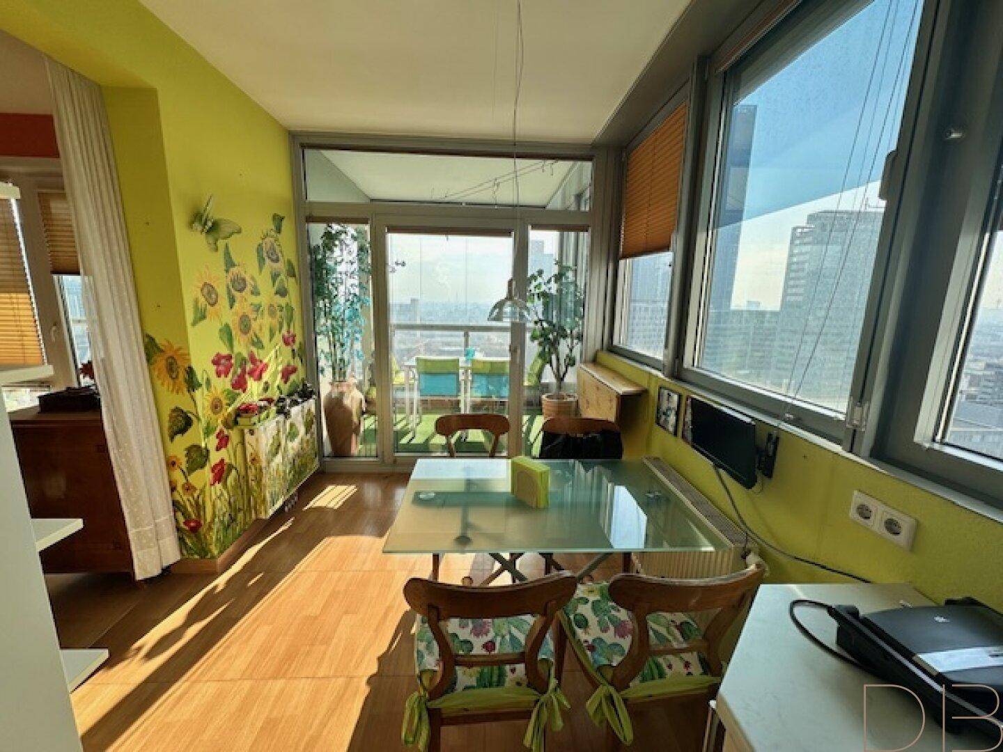 Heller Essbereich mit Glastisch, Holzboden und Zugang zu einem verglasten Balkon mit Stadtblick.