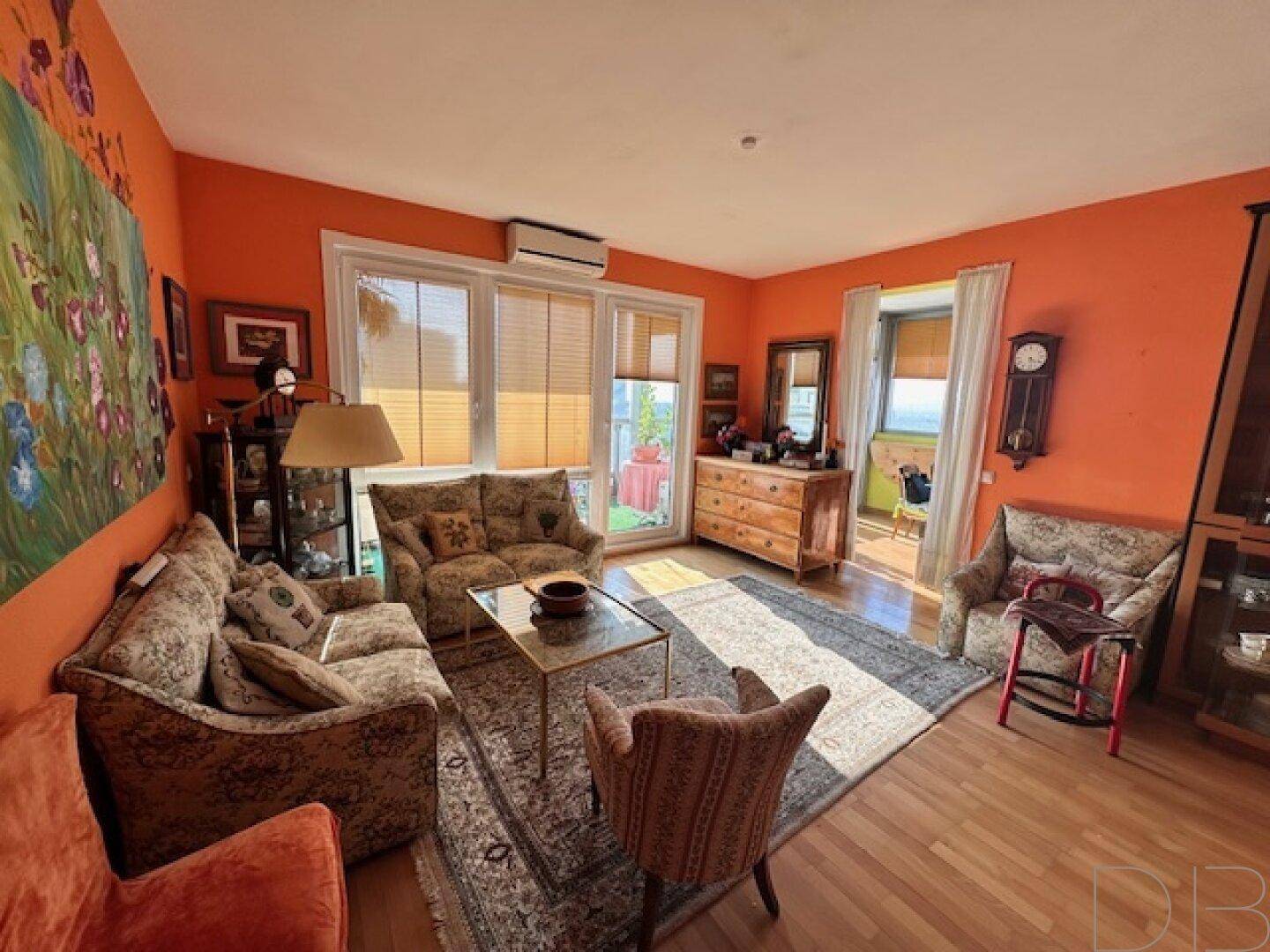 Gemütliches Wohnzimmer mit orangefarbenen Wänden, klassischen Sofas und Zugang zu einem Außenbereich.