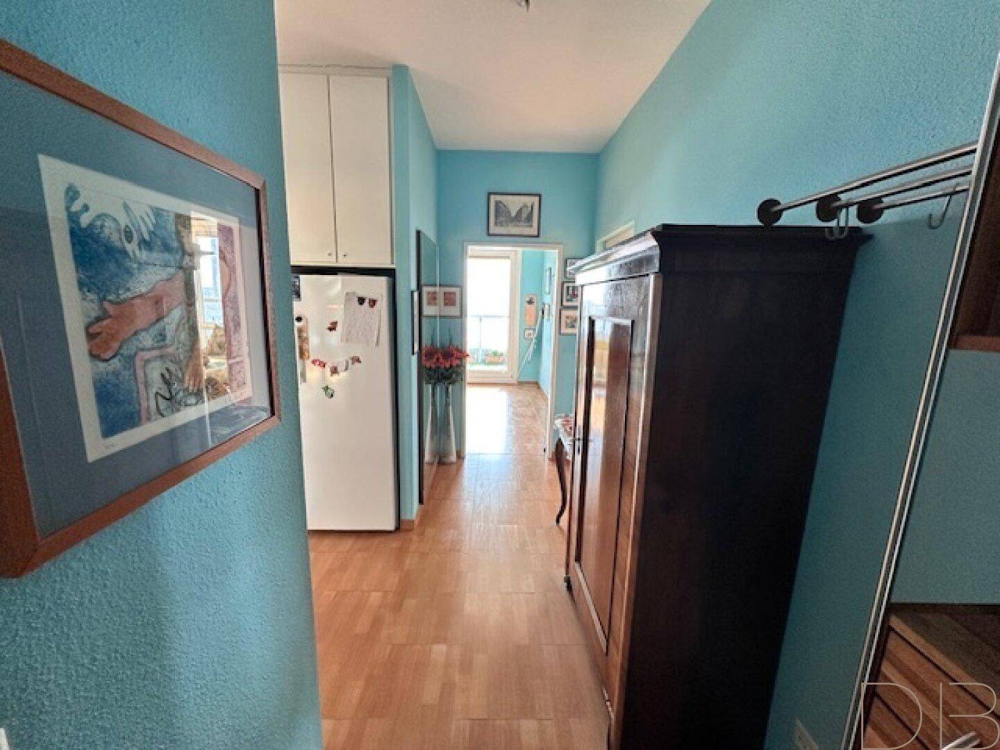 Langer Flur mit blauen Wänden, Holzfußboden und einem integrierten Kühlschrank.