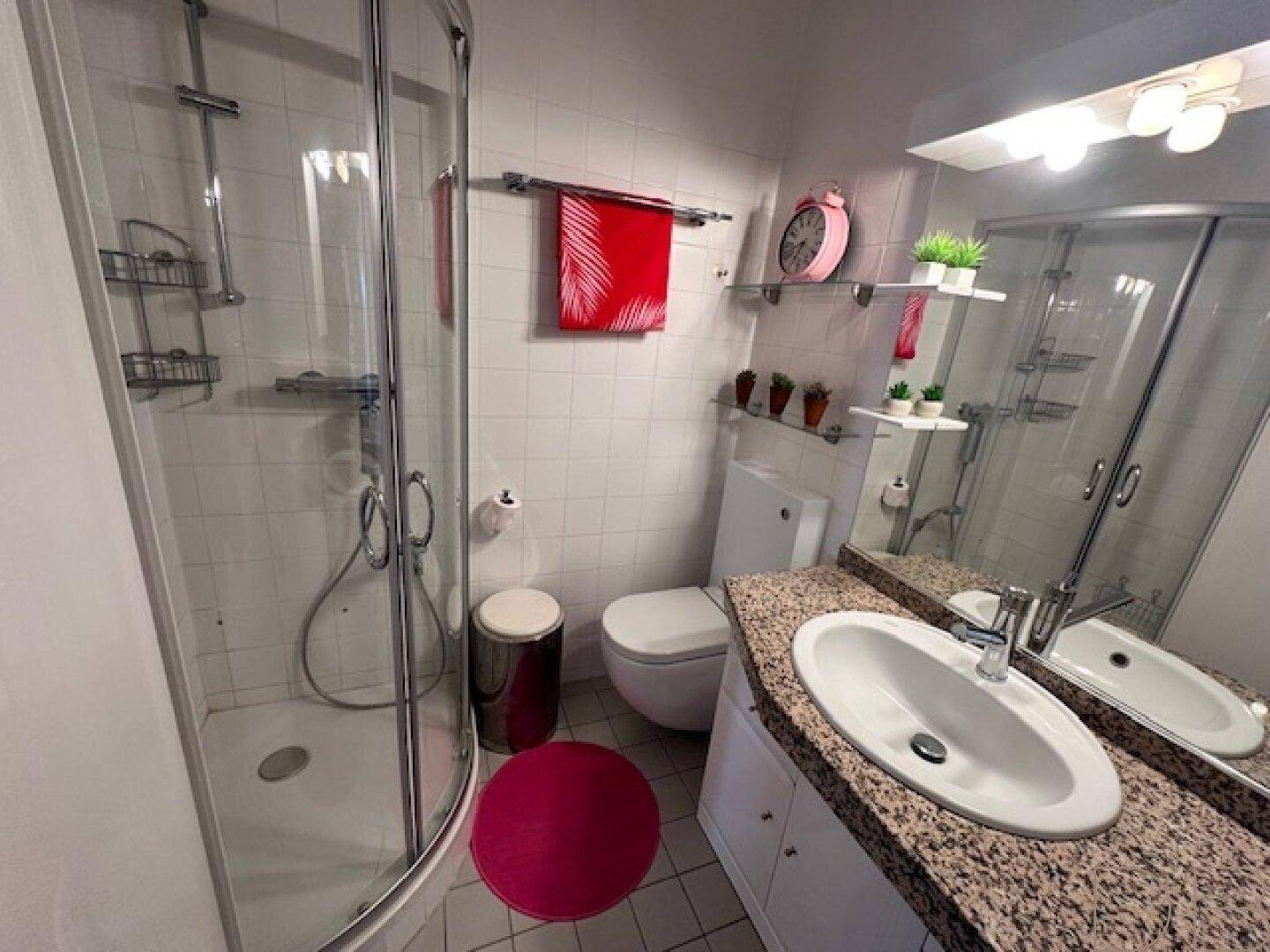 Modernes Badezimmer mit weiß gefliesten Wänden, Duschkabine und Waschtisch mit Granitplatte.
