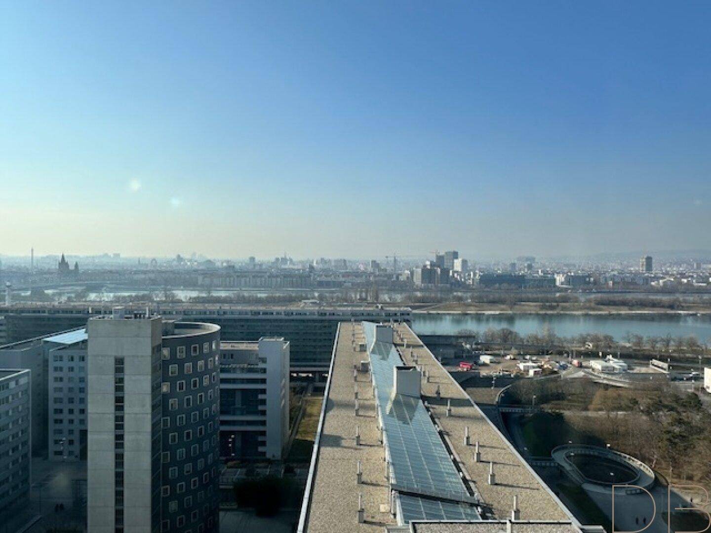 Weitläufige Stadtansicht mit Fluss, modernen Gebäuden und klarem blauem Himmel.