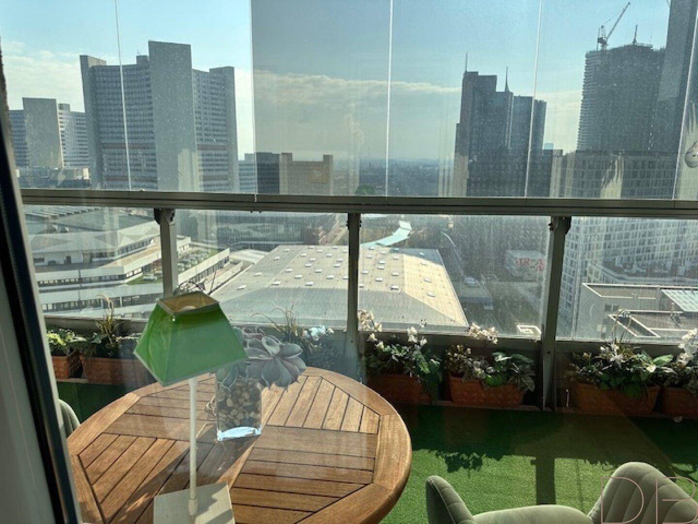 Verglaster Balkon mit Kunstrasen und Sitzgelegenheiten bietet einen weiten Blick auf die Stadt.