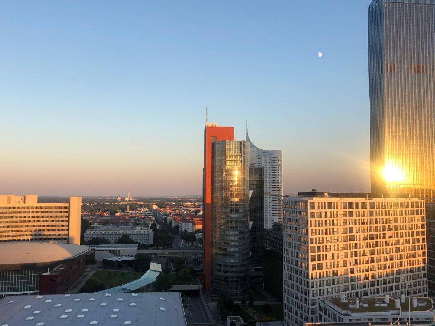 Stadtpanorama bei Sonnenuntergang mit modernen Gebäuden und einem sichelförmigen Mond am Himmel.