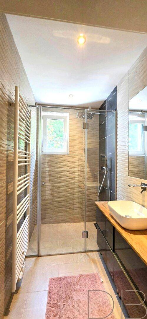 Modernes Badezimmer mit begehbarer Dusche, beheiztem Handtuchhalter und strukturierten Wandfliesen.