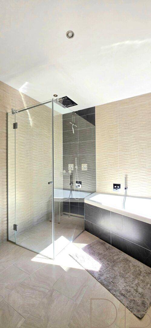 Elegantes Badezimmer mit Badewanne, Glasdusche und modernen Fliesen an den Wänden.