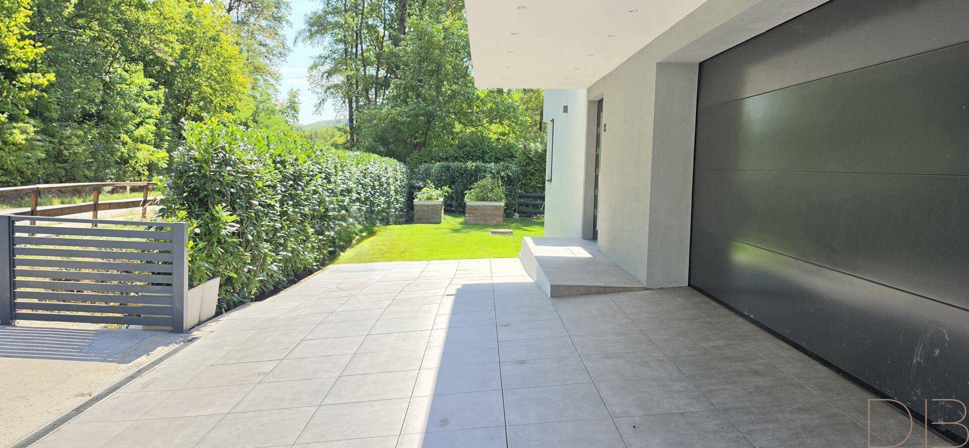 Moderne Garage mit großem Tor und gepflasterter Einfahrt, umgeben von Grünflächen.