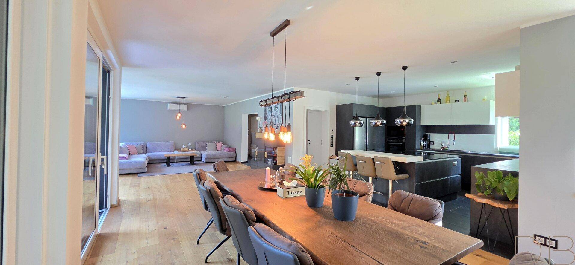 Geräumiger offener Wohn- und Essbereich mit Holztisch und moderner Küche im Hintergrund.