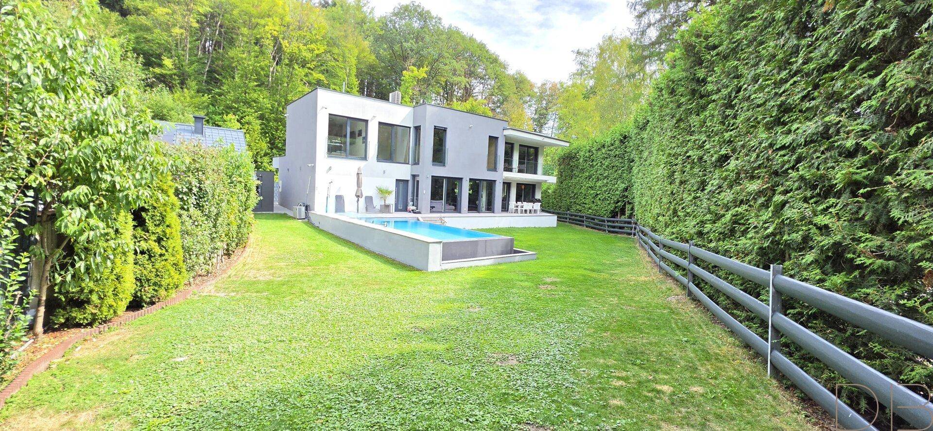 Weitläufiger Garten mit modernem Haus, Swimmingpool und üppiger grüner Hecke.