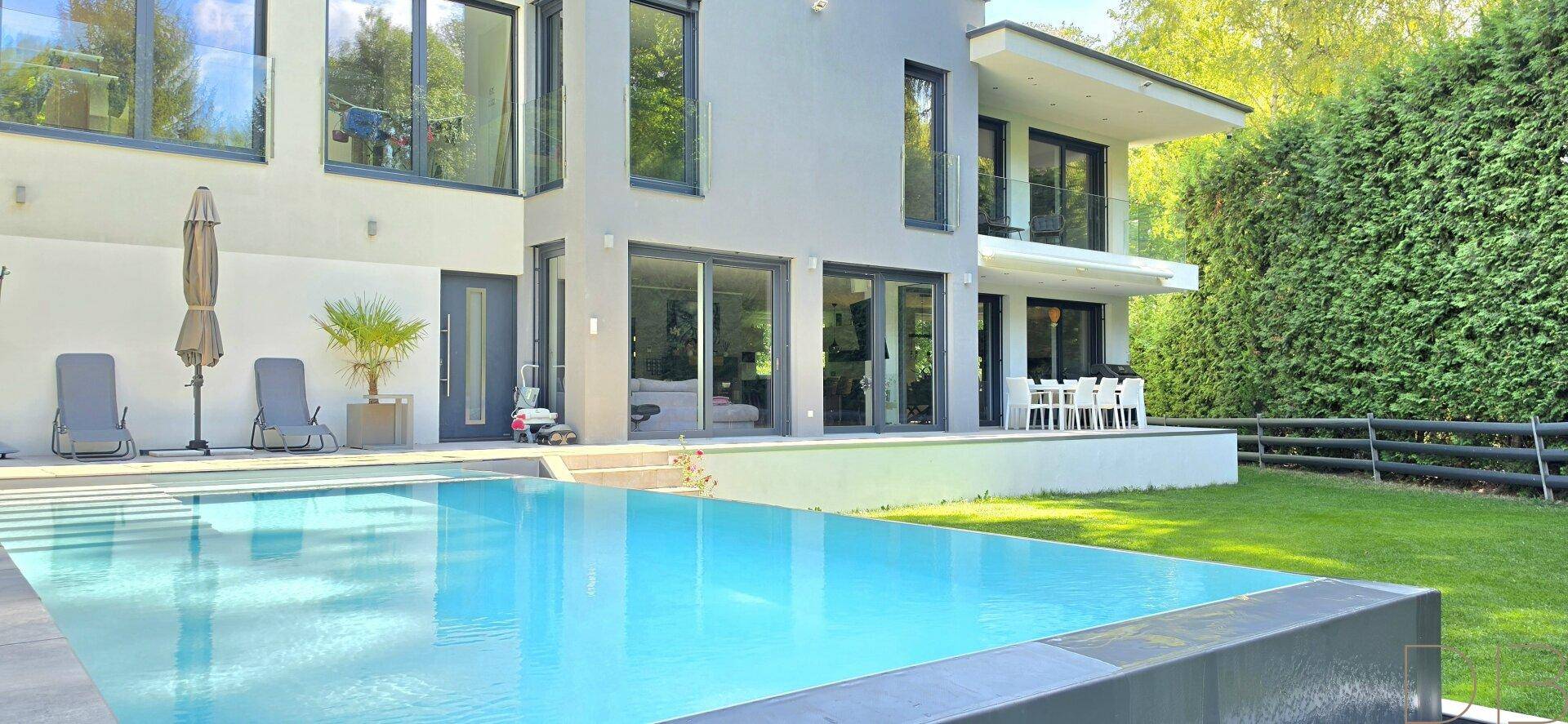 Elegante Terrasse mit Swimmingpool, Liegestühlen und Blick auf die moderne Hausfassade.