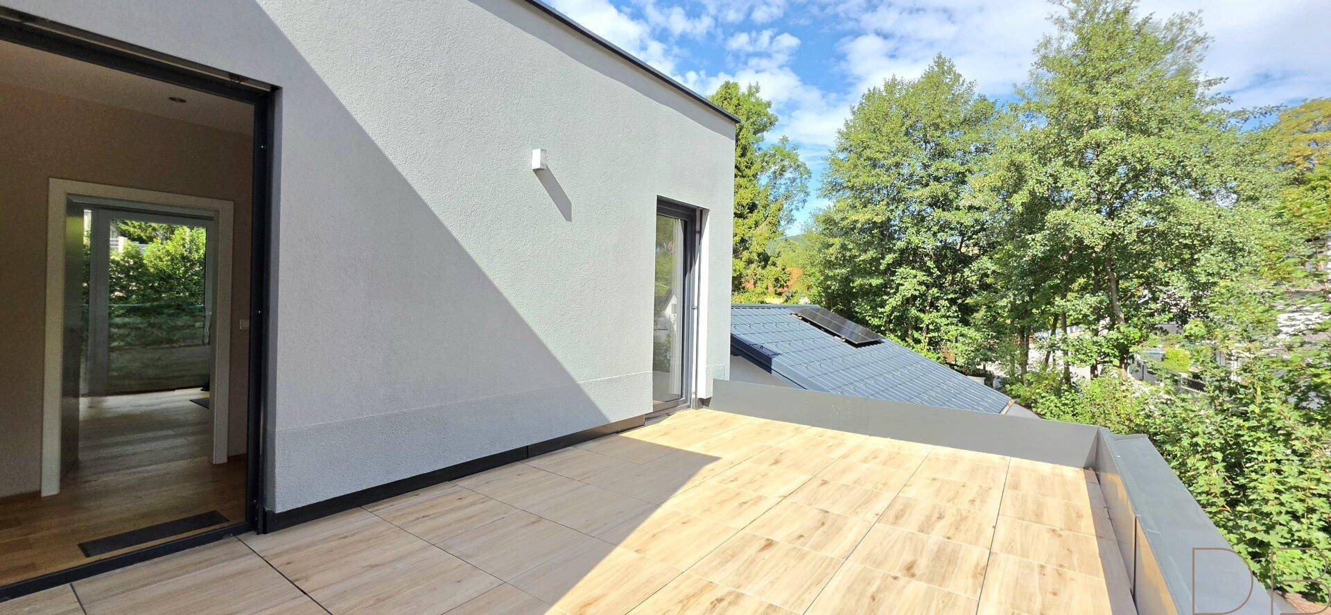 Große, sonnige Dachterrasse mit Holzboden und Blick auf die grüne Umgebung.
