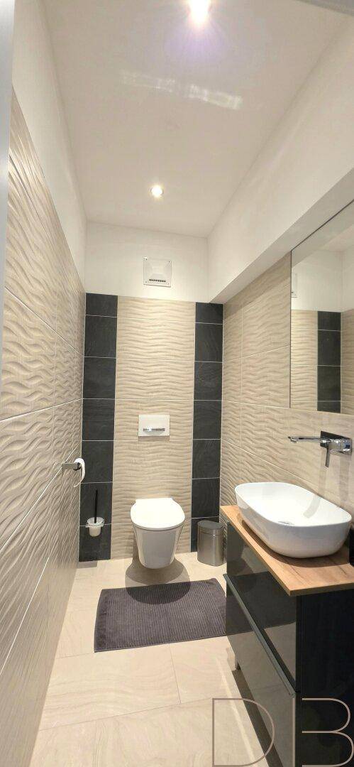 Modernes WC mit wandhängender Toilette, stilvollem Waschbecken und strukturierten Wandfliesen.