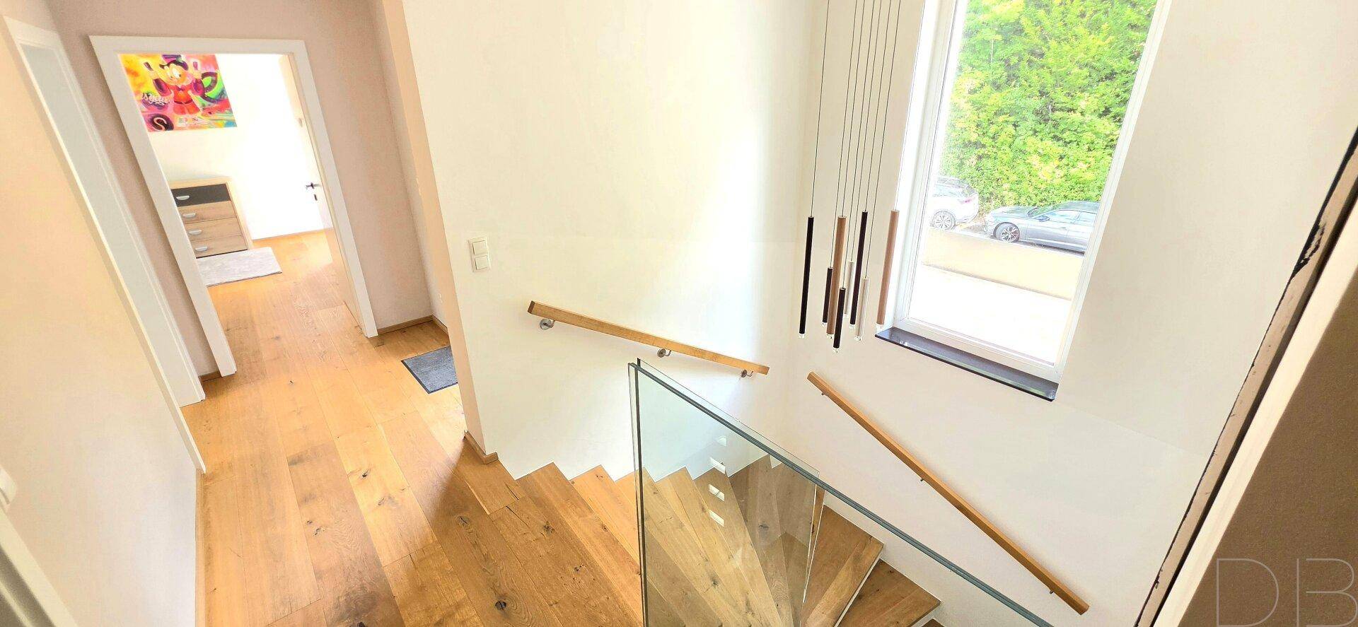 Heller Treppenaufgang mit Holzstufen, Glasgeländer und Blick auf die Umgebung.