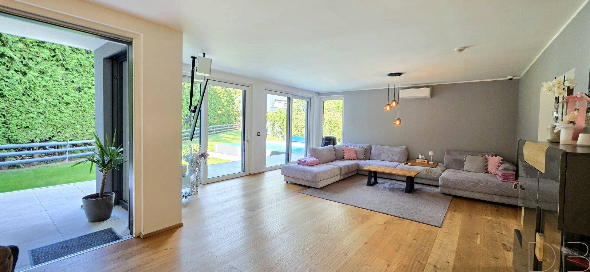 Helles Wohnzimmer mit Holzboden, großen Fenstern und Zugang zur Terrasse und zum Garten.