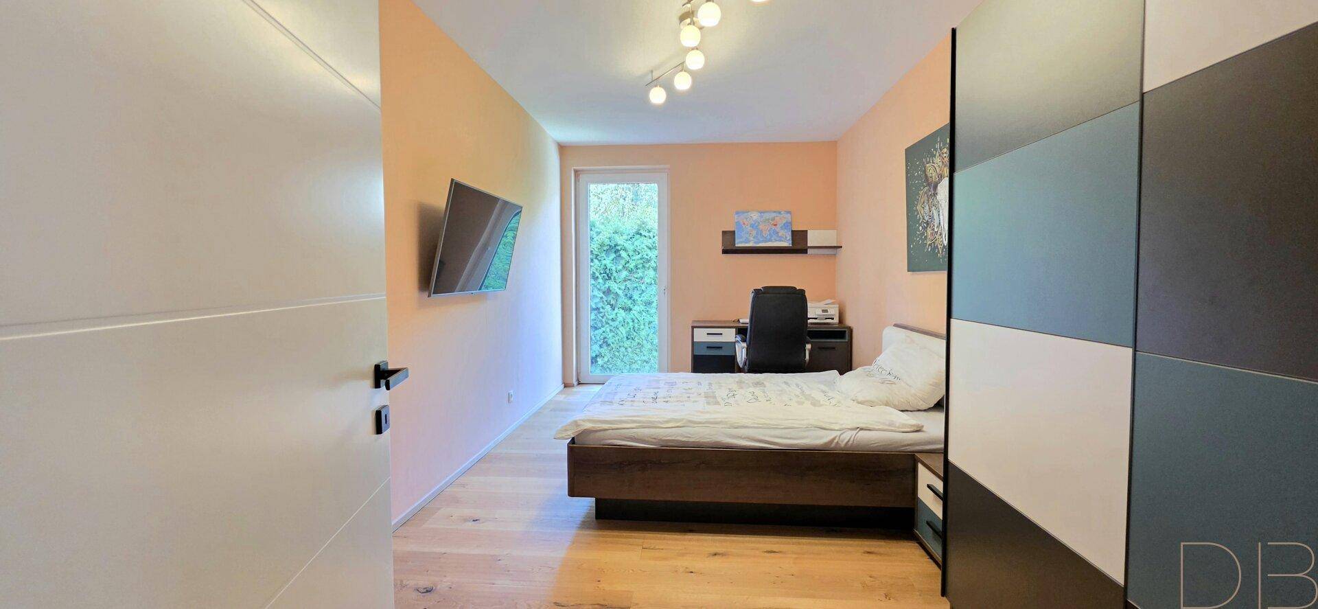 Gemütliches Schlafzimmer mit Holzboden, Schreibtisch und Zugang zu einem Balkon.