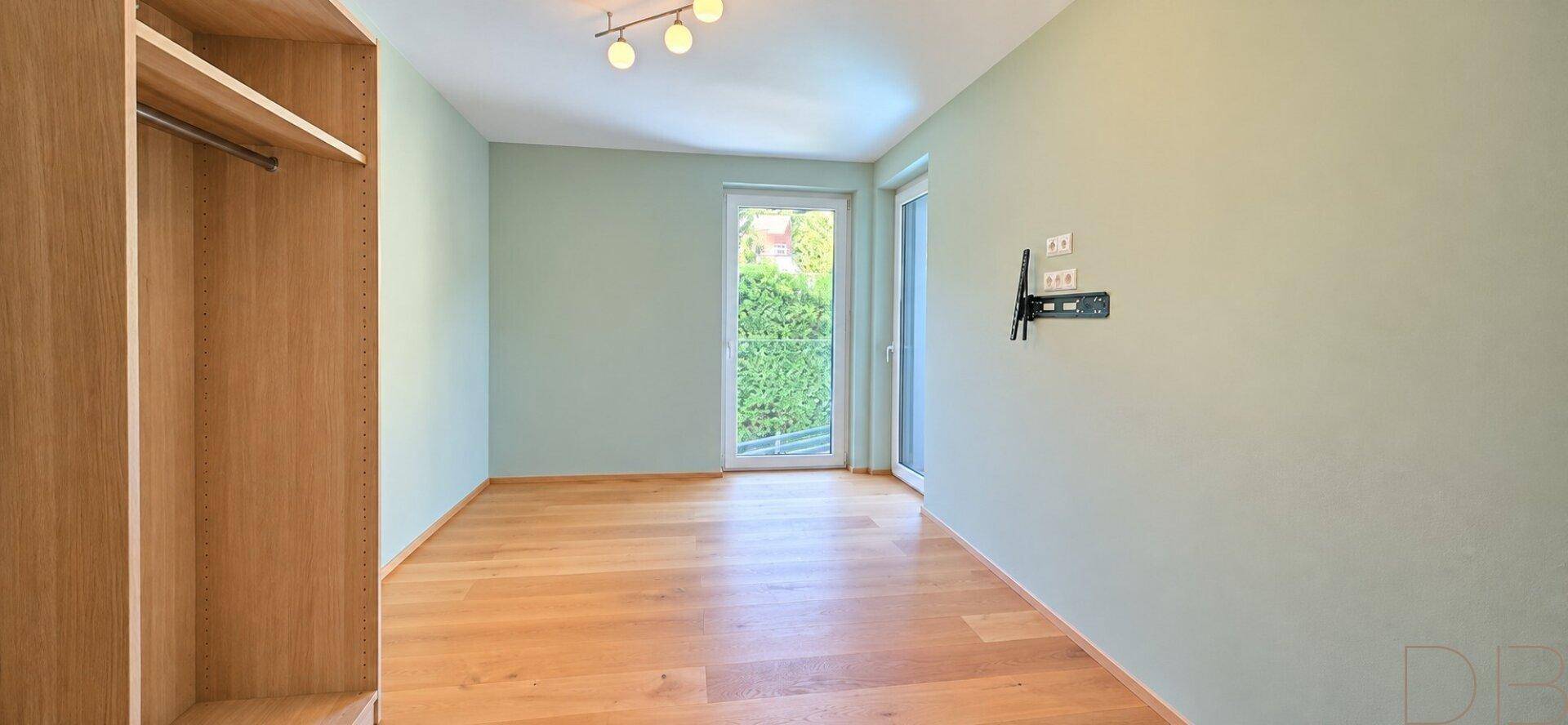 Geräumiges Schlafzimmer mit Holzboden, hellgrünen Wänden und Zugang zum Balkon.