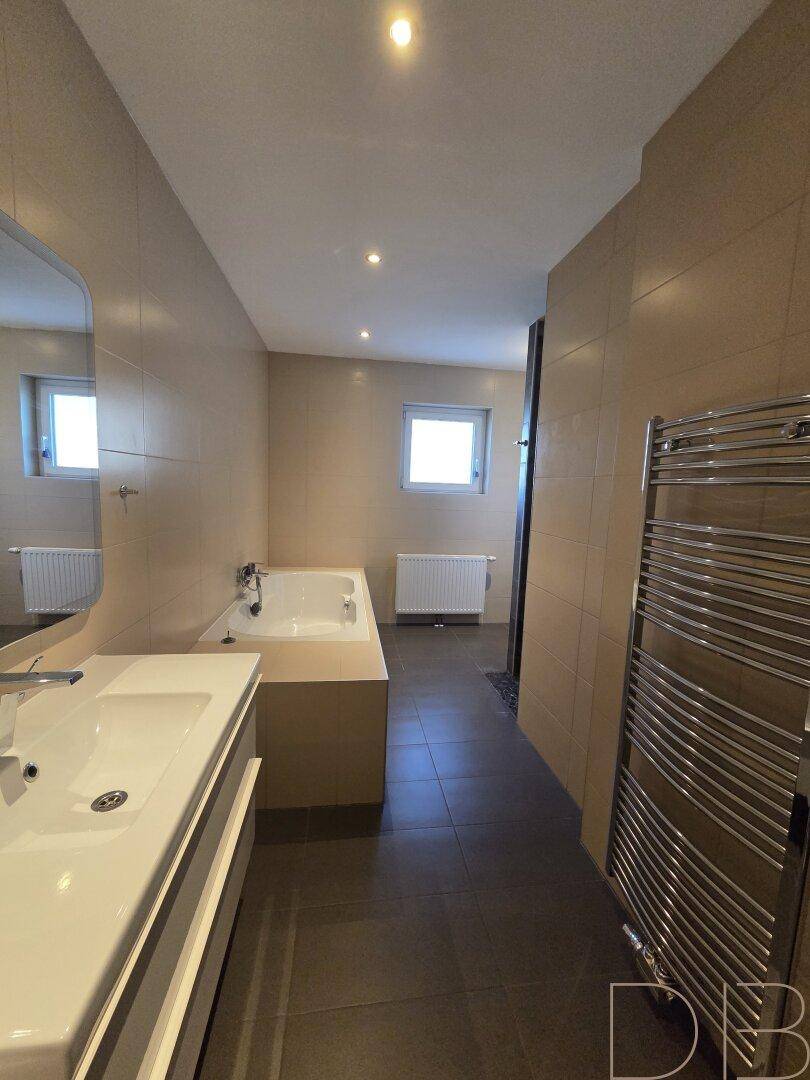 Modernes Badezimmer mit Badewanne, Dusche und beheiztem Handtuchhalter in beigen Farbtönen.