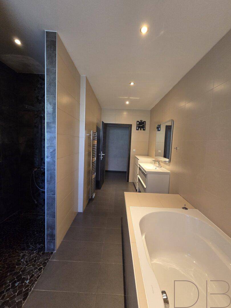 Langes Badezimmer mit Badewanne, separater Dusche und dunklem Kiesboden im Duschbereich.
