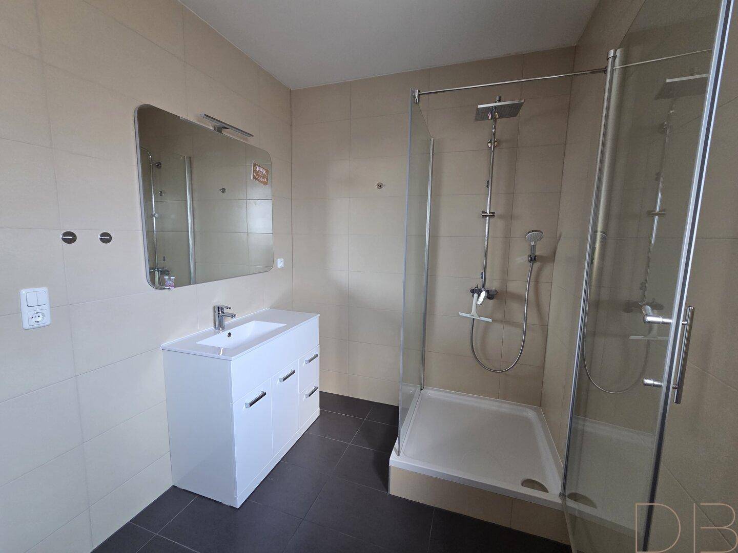 Modernes Badezimmer mit Duschkabine, Waschtisch und hellen Fliesen an Wänden und Boden.