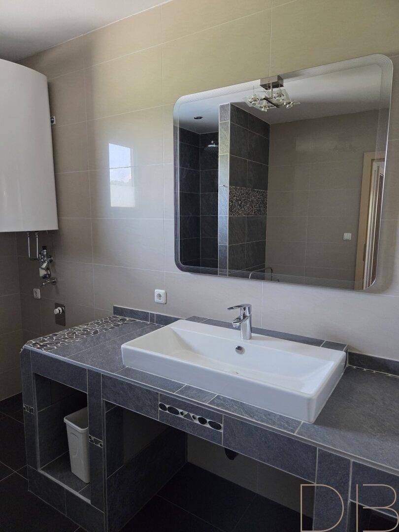 Badezimmer mit modernem Waschtisch, großem Spiegel und Boiler an der Wand.