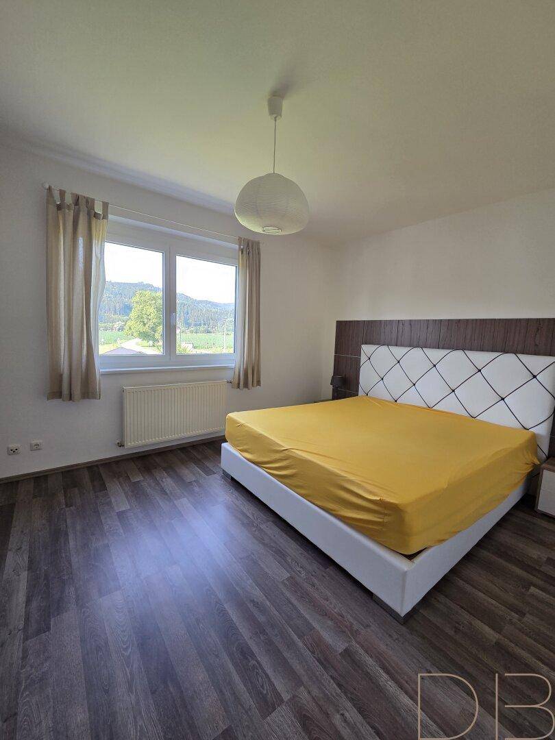 Helles Schlafzimmer mit Doppelbett, Holzboden und weitem Blick in die Natur.