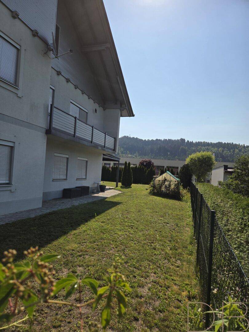 Seitlicher Gartenbereich des Hauses mit Rasenfläche, Zaun und Gewächshaus.