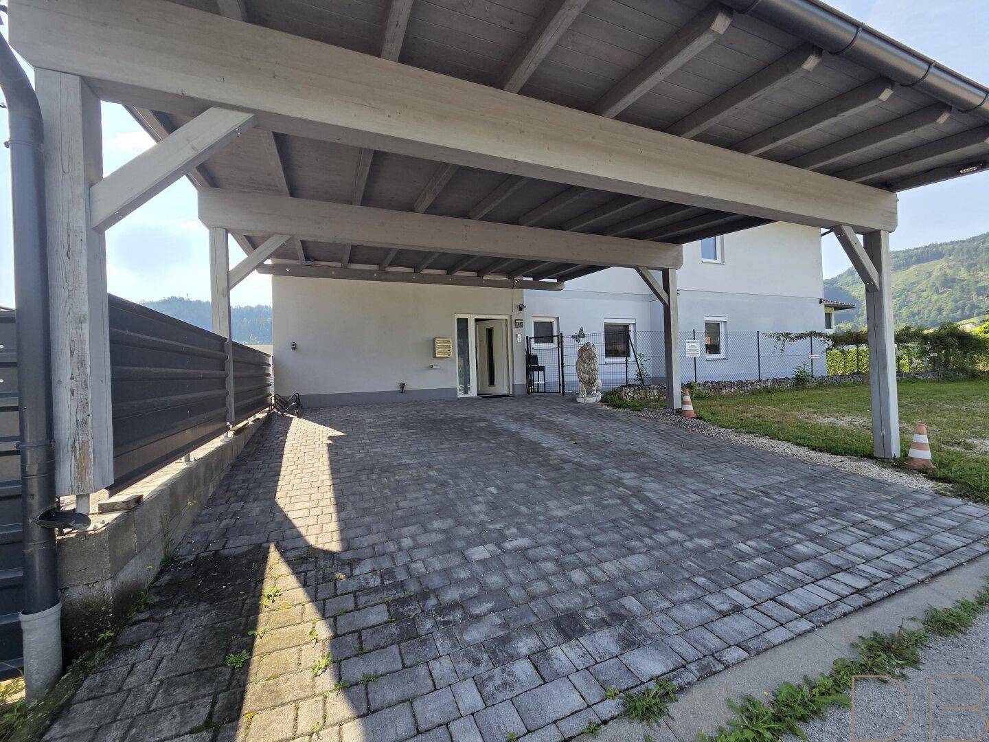 Überdachter Carport-Bereich mit gepflasterter Einfahrt vor dem Haus.