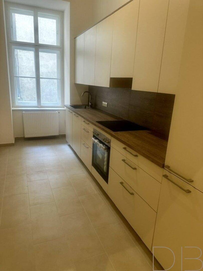 Moderne Einbauküche mit hellen Schränken, Holz-Arbeitsplatten und integrierten Geräten.