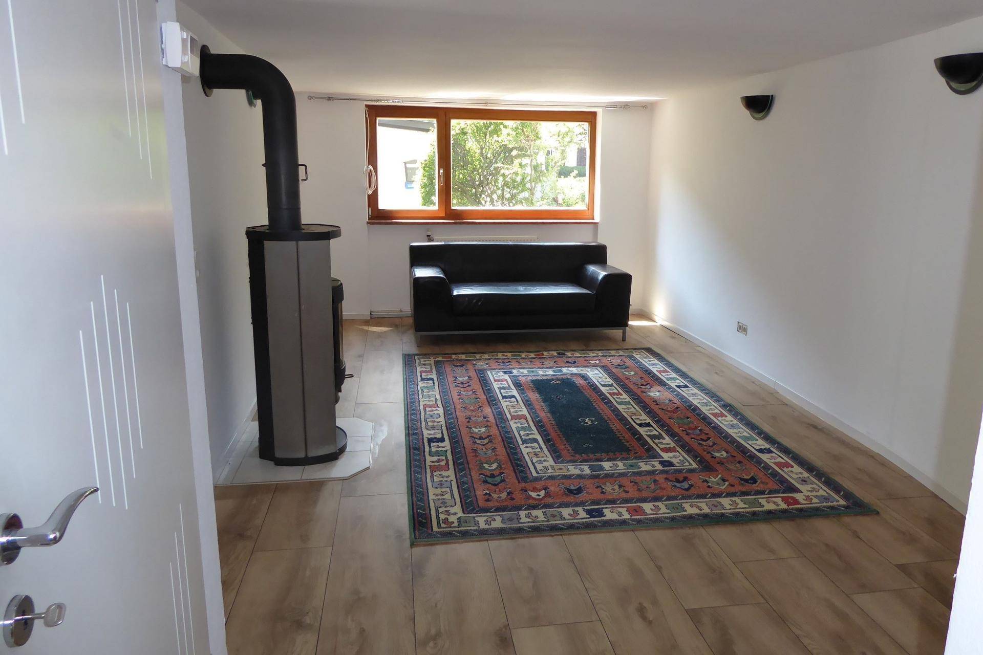 Helles Wohnzimmer mit Holzboden, einem Kaminofen und einem Teppich als Blickfang.