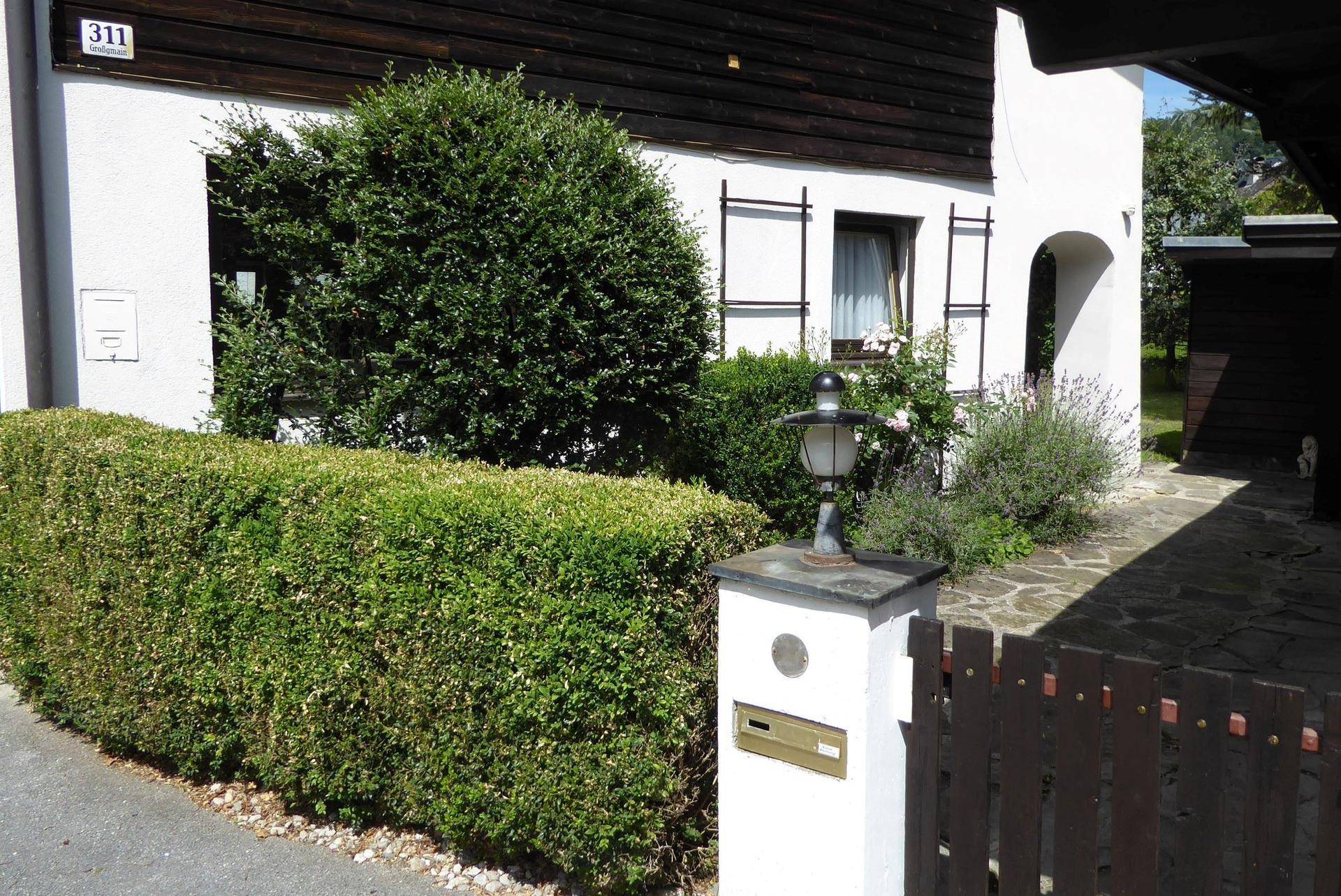 Vorderansicht des Hauses mit gepflegter Hecke, Zaun und einem Briefkasten am Eingang.