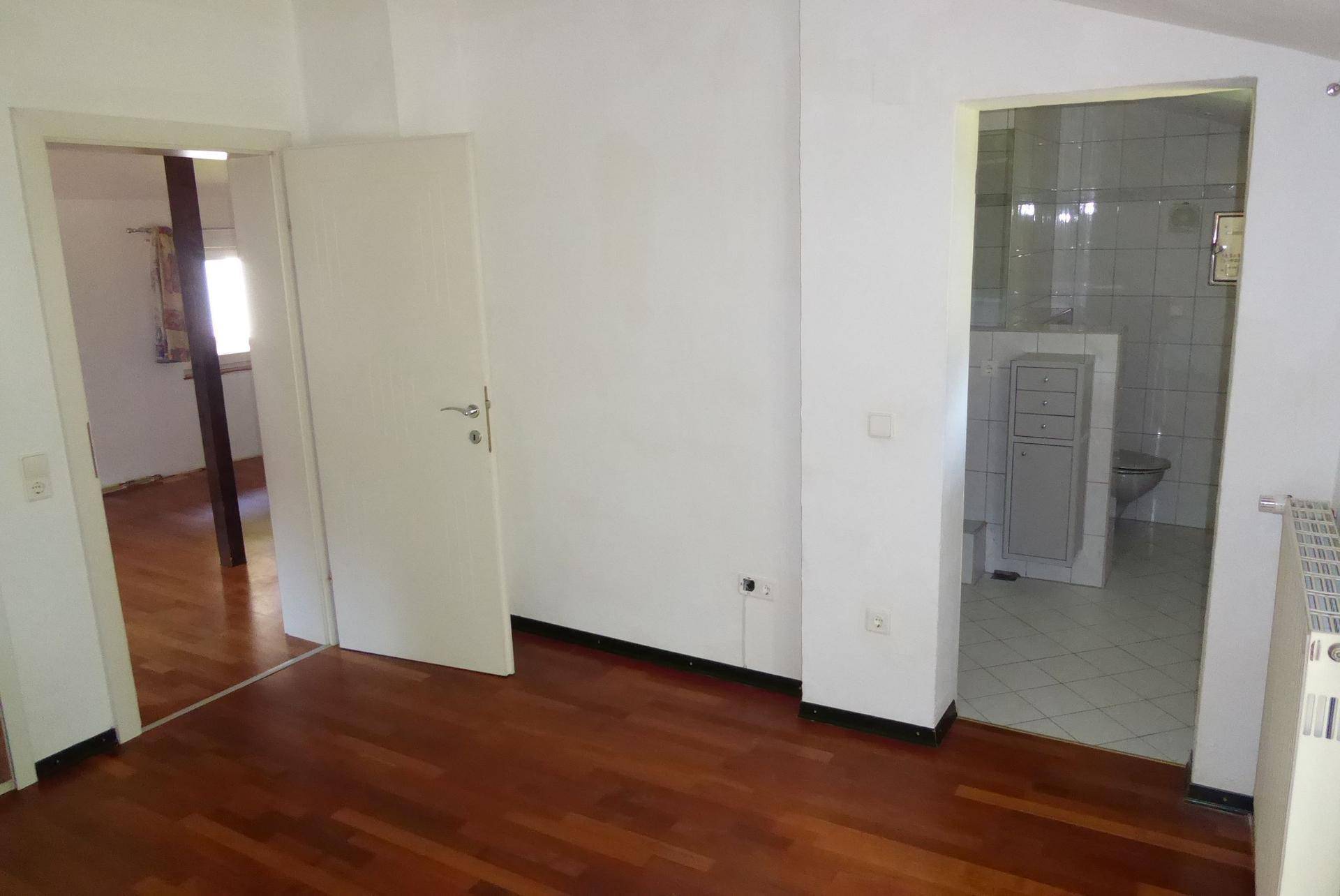 Dachgeschossraum mit Holzboden und Zugang zu einem gefliesten Badezimmer.