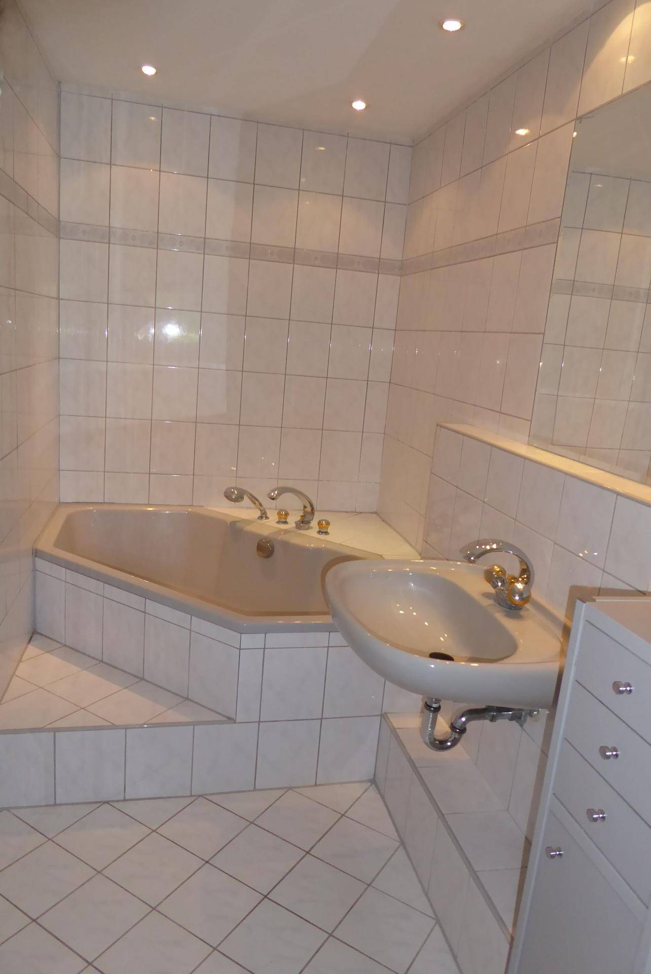 Gefliestes Badezimmer mit Eckbadewanne und einem einzelnen Waschbecken.