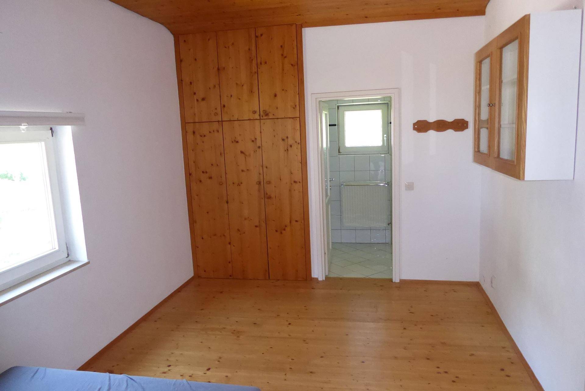 Schlafzimmer mit Holzboden, Einbauschränken und Zugang zu einem Badezimmer.