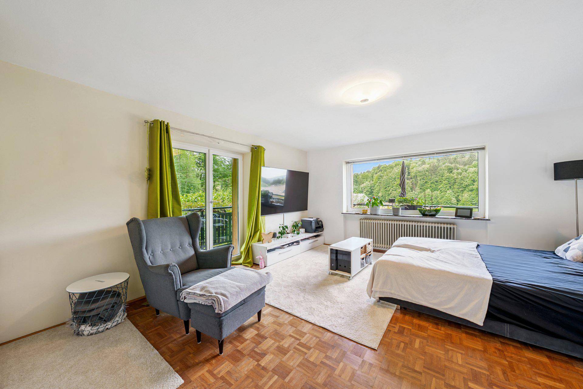 Gemütlicher Wohnbereich mit Parkettboden, großem Fenster und Zugang zu einem Balkon.
