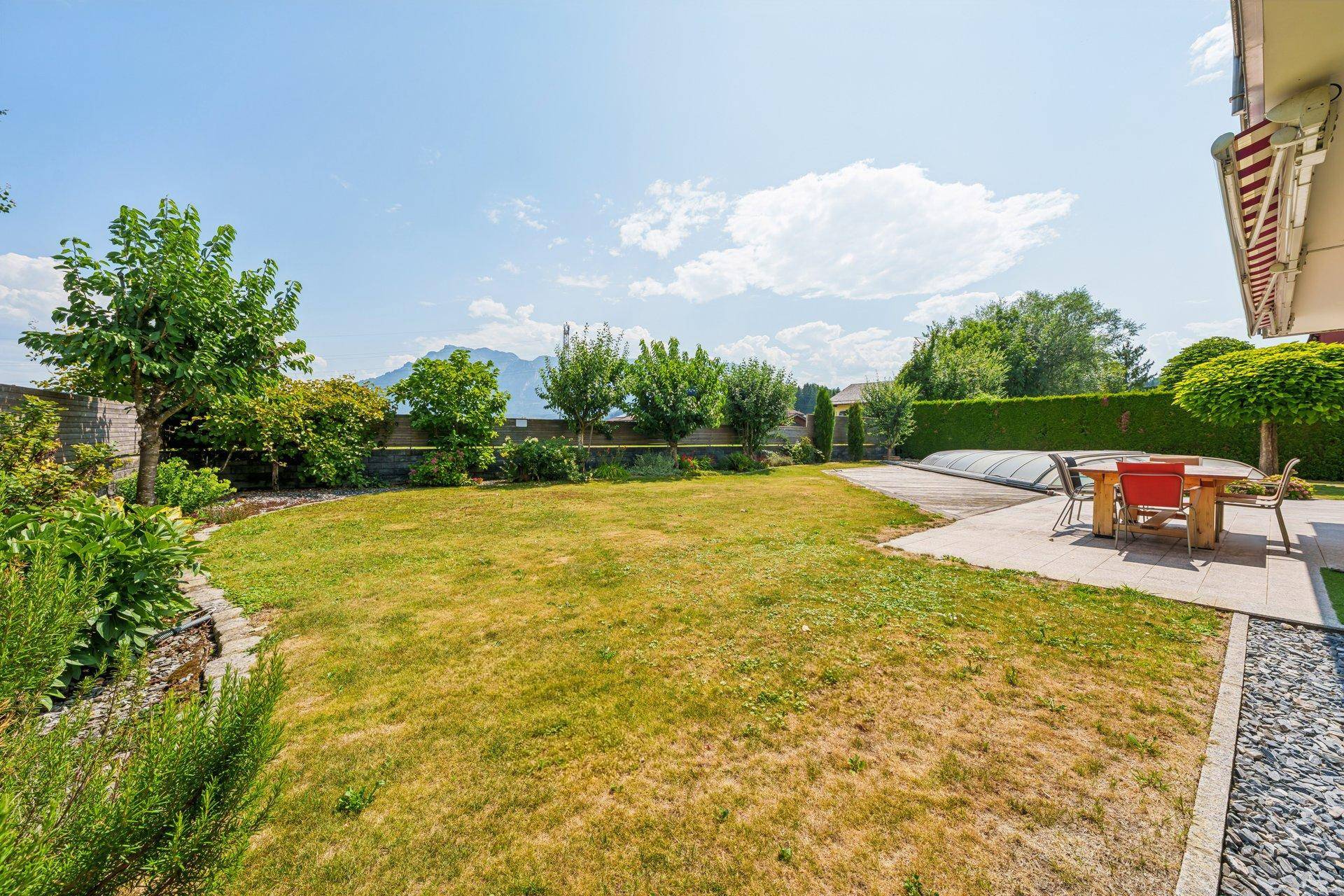 Gepflegte Gartenanlage mit Rasenfläche, Terrasse, Pool und Bergblick im Hintergrund.