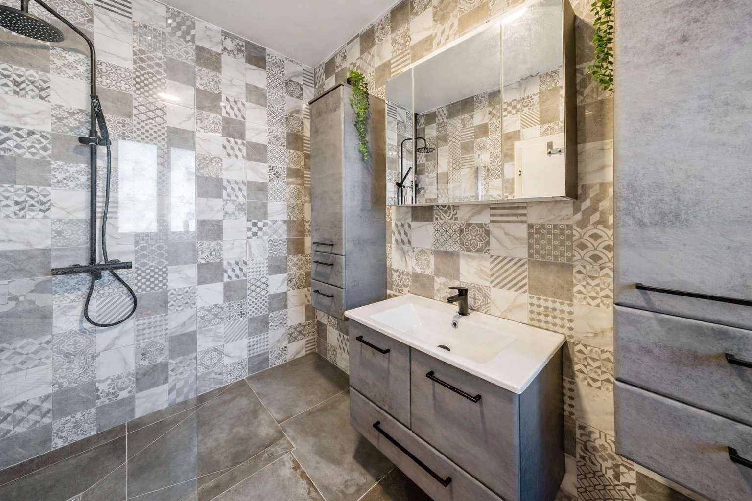 Modernes Badezimmer mit begehbarer Dusche, Waschtisch und gemusterten Fliesen.
