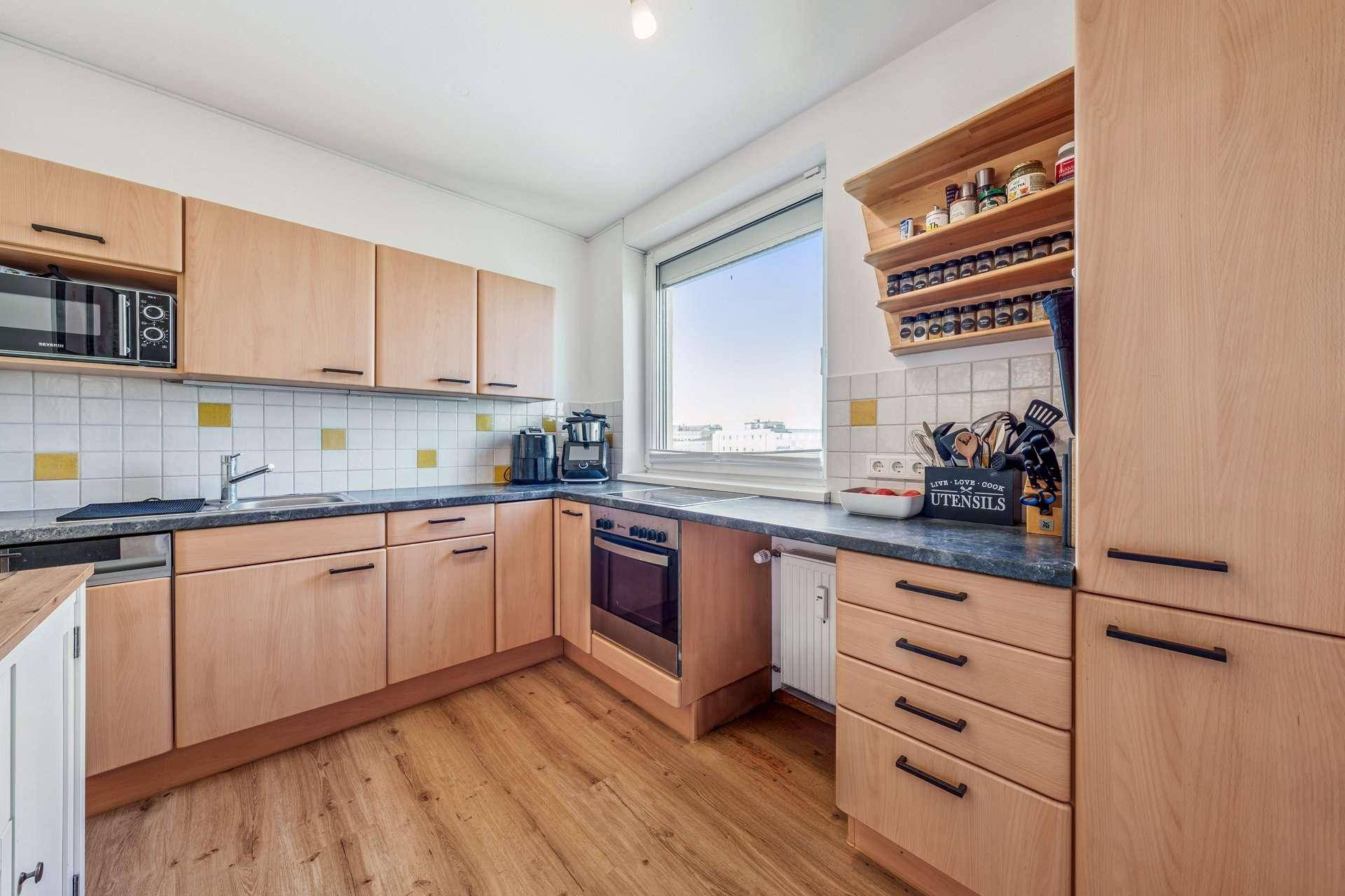 Funktionale Küche mit hellen Holzschränken, dunkler Arbeitsplatte und Fenster mit Ausblick.